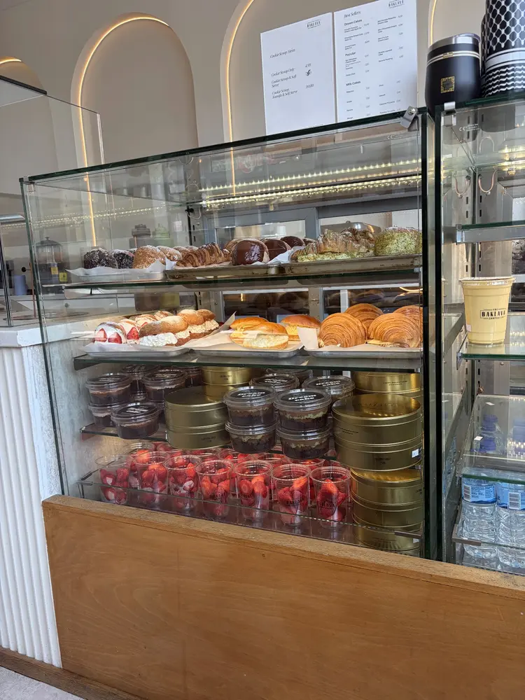 Glass counter stacked with croissants, filled buns, dream cakes in gold tins and cups of strawberries